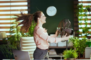 Sürdürülebilir iş yeri. Modern yeşil ofisteki 40 yıllık modern kadın çalışanın elektrikli yelpazesiyle gülümsemesi..