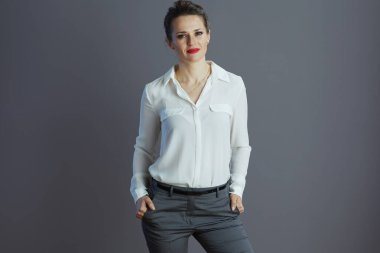 Beyaz bluzlu, modaya uygun orta yaşlı iş kadını gri arka planda izole edilmiş..