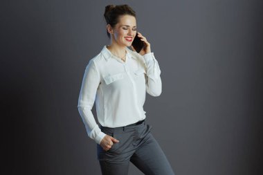 Kırk yaşında, beyaz bluzlu, gri arka planda izole edilmiş bir cep telefonu kullanan küçük işletme sahibi bir kadın..