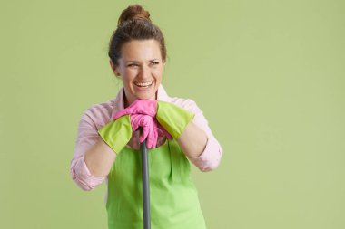 Bahar temizliği. Yeşil önlüklü, lastik eldivenli, yeşil arka planda paspaslı 40 yaşında mutlu bir kadın..