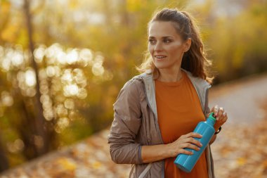 Merhaba sonbahar. Parkta elinde bir şişe suyla fitness kıyafetleri içinde son moda orta yaşlı bir kadın..