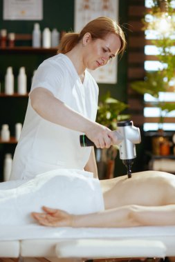 Sağlık hizmeti zamanı. Masaj dolabında masaj tabancasıyla masaj terapisti masaj masasına masaj yapıyor..