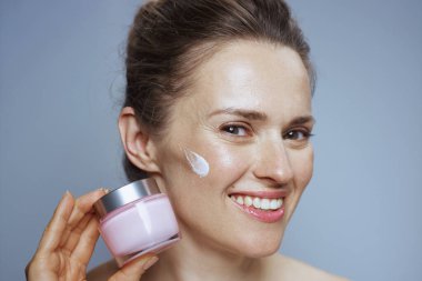 Mavi arka planda kozmetik krem kavanozu olan mutlu genç bir kadın..