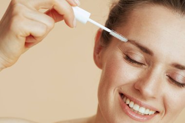 Bej arka planda kaş fırçası olan mutlu orta yaşlı kadın..