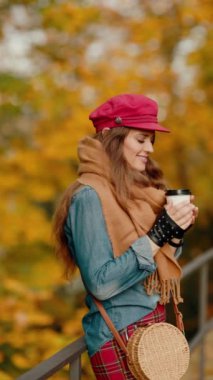 Merhaba sonbahar. Şehir parkında kırmızı şapkalı, şallı, eldivenli, çantalı ve kahveli 40 yaşında mutlu bir stil sahibi kadın..