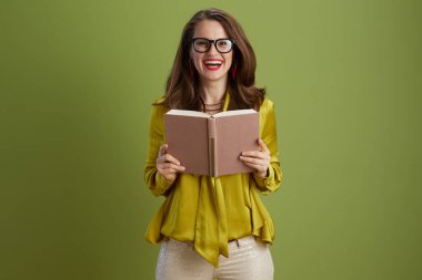 Yeşil arka planda yeşil bluzlu ve kitaplı gözlüklü, gülümseyen modern kadın..