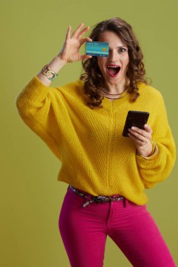 40 yaşında, sarı kazaklı, kredi kartı ve akıllı telefonlu, yeşil arka planlı bir kadın..