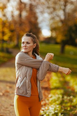 Merhaba sonbahar. Parkta esneme hareketleri yapan orta yaşlı şık bir kadın..