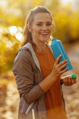 Merhaba sonbahar. Parkta elinde su şişesiyle spor kıyafetleri içinde gülümseyen 40 yaşındaki bir kadının portresi..