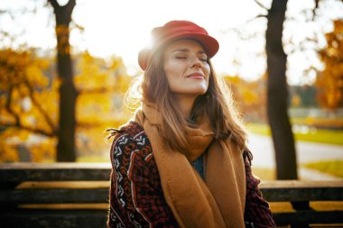 Merhaba sonbahar. Şehir parkında bankta oturan kırmızı şapkalı, orta yaşlı, rahat bir kadın..