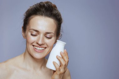 Mavi arka planda kozmetik krem kavanozuyla gülümseyen orta yaşlı kadın..