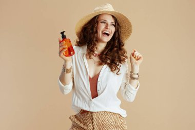 Plaj tatili Beyaz bluzlu mutlu bir kadın ve bej arka planda saç bakım ürünü ve hasır şapkalı bir şort..