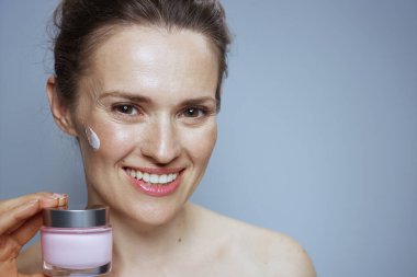 Mavi arka planda kozmetik krem kavanozu olan mutlu modern kadın..