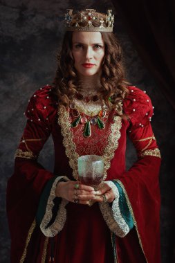 Kırmızı elbiseli, tacı koyu gri arka planda olan ortaçağ kraliçesi..