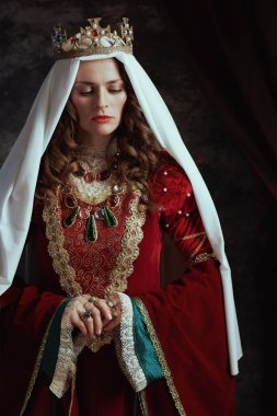 Kırmızı elbiseli, peçeli ve tacı koyu gri arka planlı ortaçağ kraliçesi..