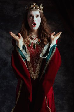 Kırmızı elbiseli, beyaz makyajlı ve tacı koyu gri arkaplanlı ortaçağ kraliçesi..