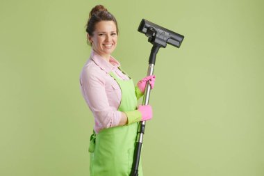 Bahar temizliği. Yeşil önlüklü, lastik eldivenli, yeşil elektrikli süpürgeyle izole edilmiş 40 yıllık mutlu modern kadın..