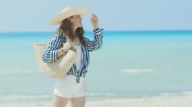 Kumsalda saman torbası ve hasır şapkalı mutlu modern bir kadın..