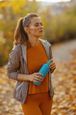 Merhaba sonbahar. Parkta elinde su şişesi olan orta yaşlı, modern bir kadın..