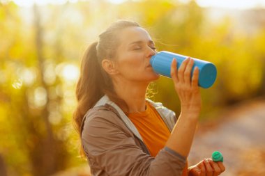 Hello autumn. elegant woman in fitness clothes in the park with bottle of water. clipart