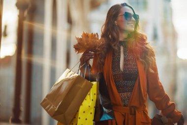 Merhaba sonbahar. Kahverengi trençkotlu, alışveriş torbalı, güz sarısı yapraklı, şık bir kadın..