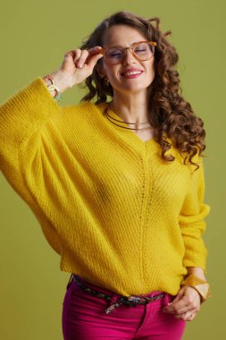 Sarı süveter ve gözlüklerle yeşil üzerine izole edilmiş gülümseyen modern kadın..