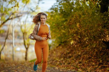 Hello autumn. modern female in fitness clothes in the park running. clipart