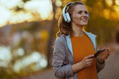 Merhaba sonbahar. Parkta kulaklıkları olan orta yaşlı, mutlu bir kadın..