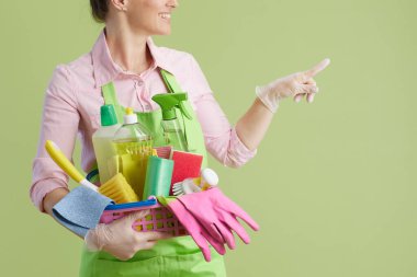 Bahar temizliği. Yeşil önlüklü, yeşil eldivenli, gülümseyen orta yaşlı ev kadınına yakın plan ve fotokopi alanını gösteren temizlik ürünleri sepeti..