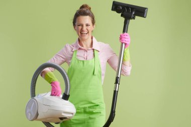 Bahar temizliği. Yeşil önlüklü, lastik eldivenli, yeşil arka plan süpürgesine gülümseyen 40 yaşında bir kadın..