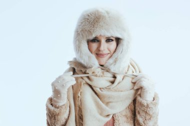 Beyaz arka planda beyaz eldivenlerle izole edilmiş kürk şapkalı ve kışlık ceketli gülümseyen modern kadın..