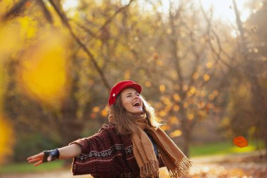 Merhaba sonbahar. Kırmızı şapkalı, eşarplı ve eldivenli zarif bir kadın şehir parkında neşe içinde..