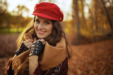 Merhaba sonbahar. Şehir parkında kırmızı şapkalı, eşarplı ve eldivenli gülümseyen moda kadının portresi..