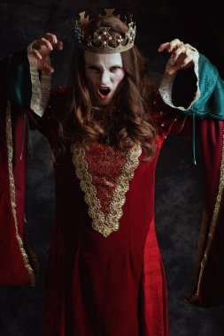 Kırmızı elbiseli, beyaz makyajlı ve tacı koyu gri arka planda korkunç bir ortaçağ kraliçesi..