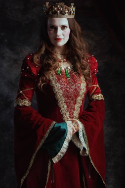 Kırmızı elbiseli, beyaz makyajlı ve tacı koyu gri arka planda olan ortaçağ kraliçesi..