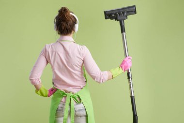Bahar temizliği. Arkadan, yeşil önlüklü, lastik eldivenli, kulaklıklı, elektrikli süpürgeli, modern orta yaşlı bir kadın görülüyor..