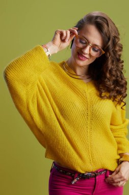 Sarı süveter ve gözlüklü yeşil arka planlı 40 yaşında mutlu bir kadın..