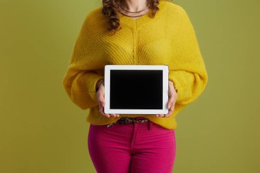 Sağlıklı 40 yaşındaki kadına yakın çekim sarı süveterli yeşil arka planda tableti boş gösteren bir tablet..