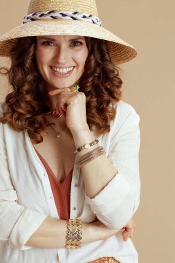 Plaj tatili Mutlu modern 40 yaşındaki beyaz bluzlu ve şortlu kadın hasır şapkalı bej arka planda.