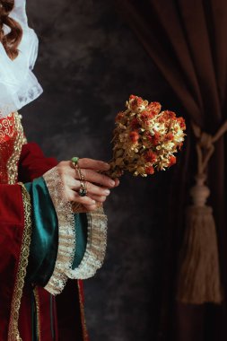 Kırmızı elbiseli, koyu gri arka planda kurumuş çiçekli ortaçağ kraliçesi..