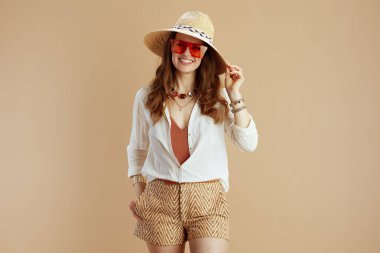 Plaj tatili Beyaz bluz ve şort giymiş zarif orta yaşlı ev hanımı bej arka planda yaz şapkası ve güneş gözlüğü takıyor..