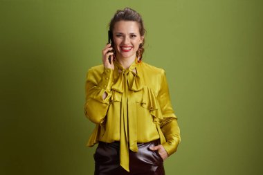 Yeşil arka planda, yeşil bluzlu, akıllı telefonlu, güler yüzlü bir kadın..