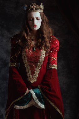 Kırmızı elbiseli, beyaz makyajlı ve tacı koyu gri arka planda olan ortaçağ kraliçesi..