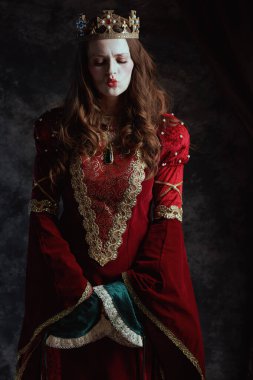 Kırmızı elbiseli, beyaz makyajlı ve tacı koyu gri arka planda olan ortaçağ kraliçesi..