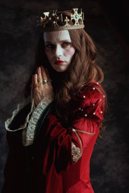 Kırmızı elbiseli, koyu gri arka planda dua eden ortaçağ kraliçesi..