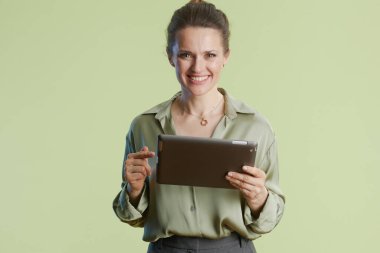30 'lu yaşlarda neşeli bir kadın tableti işaret ediyor, açık yeşil arka planda. Profesyonel bir sunum ya da gelişigüzel bir teknik etkileşim.
