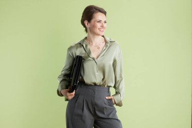 Açık yeşil bluzlu ve gri pantolonlu gülümseyen bir kadın açık yeşil bir zemine karşı siyah bir portföy ile güven içinde poz veriyor. Stüdyo ışıklandırması onun mesleki davranışlarını geliştiriyor..