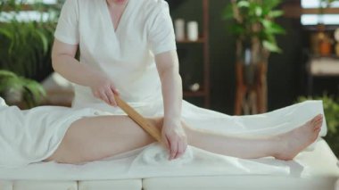 Sağlık hizmeti zamanı. Masaj kabinindeki tıbbi masaj terapistine yakın çekim. Tahta masaj çubuğu, müşterilere bacak masajı..
