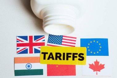 Önemli dünya ekonomilerinin bayrakları beyaz bir şişenin yanında kalın sarı bir 'TARIFFS' etiketinin altında duruyor, ticari kısıtlamaların baskısını çağrıştırıyor..