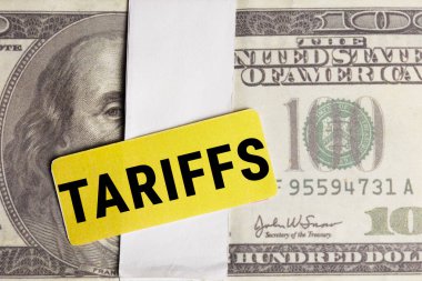 Sarı TARIFFS etiketi, mali etkileri ve küresel ticaret gerilimlerini vurgulayan 100 dolarlık bir banknota yerleştirildi.